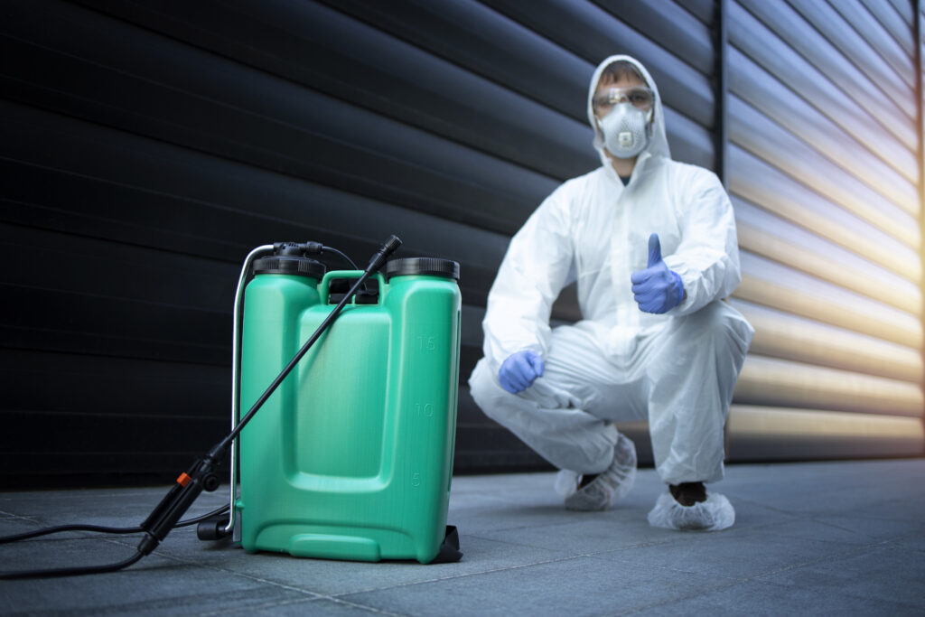 exterminateur en uniforme de protection blanc debout par reservoir avec produits chimiques et pulverisateur